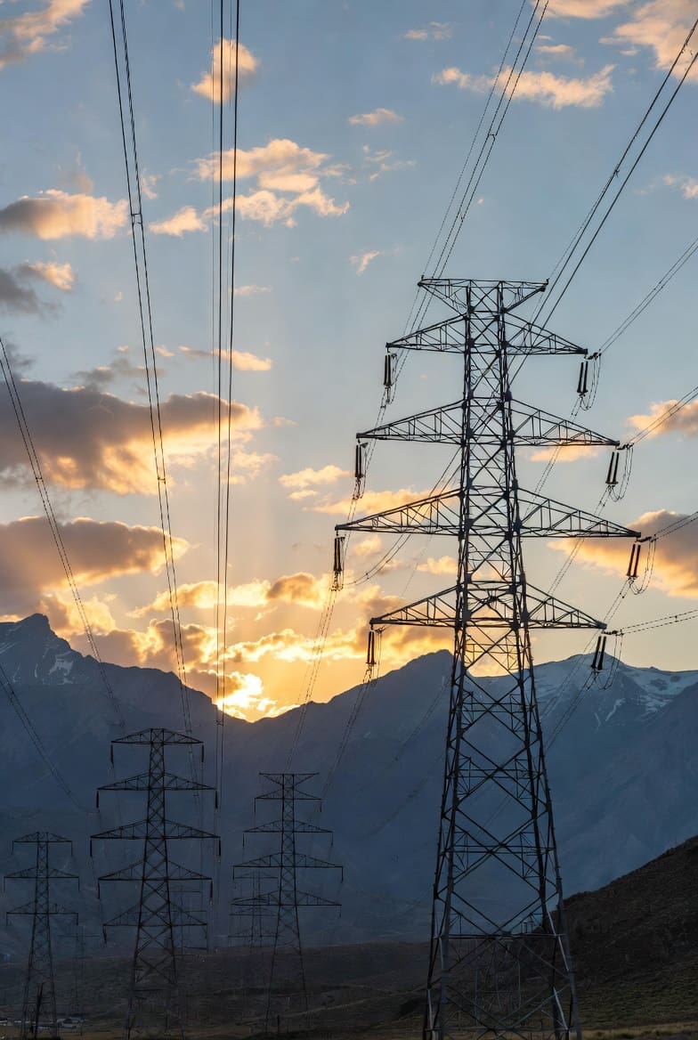 Epic wide-angle view of massive high-voltage electricity transmission towers stretching across the rugged Rocky Mountains in Canada at sunset, symbolizing the Alberta-British Columbia intertie.